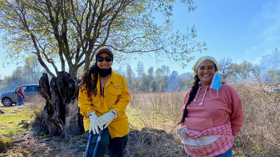 Two women smiling near a tree.