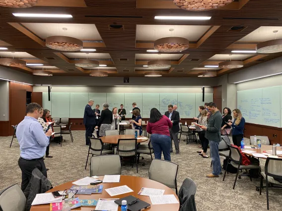 Researchers gathers in a conference room with notes on whiteboards in the background, and papers spanning the tables.