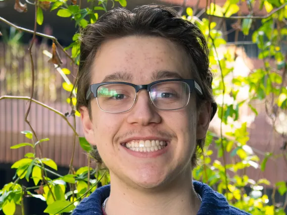 Allen in front of foliage, wearing a blue sweater and glasses