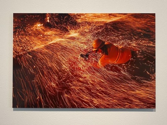 Photographer engages with the base of a fire covered in sparks and ash as the winds blow