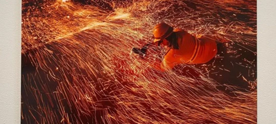 Photographer engages with the base of a fire covered in sparks and ash as the winds blow