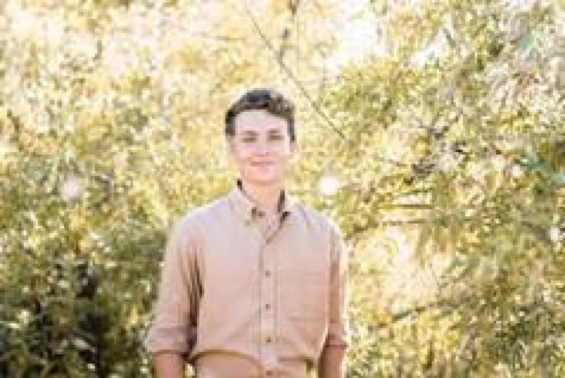 Headshot of a person standing in front of trees with the sunlight coming through.