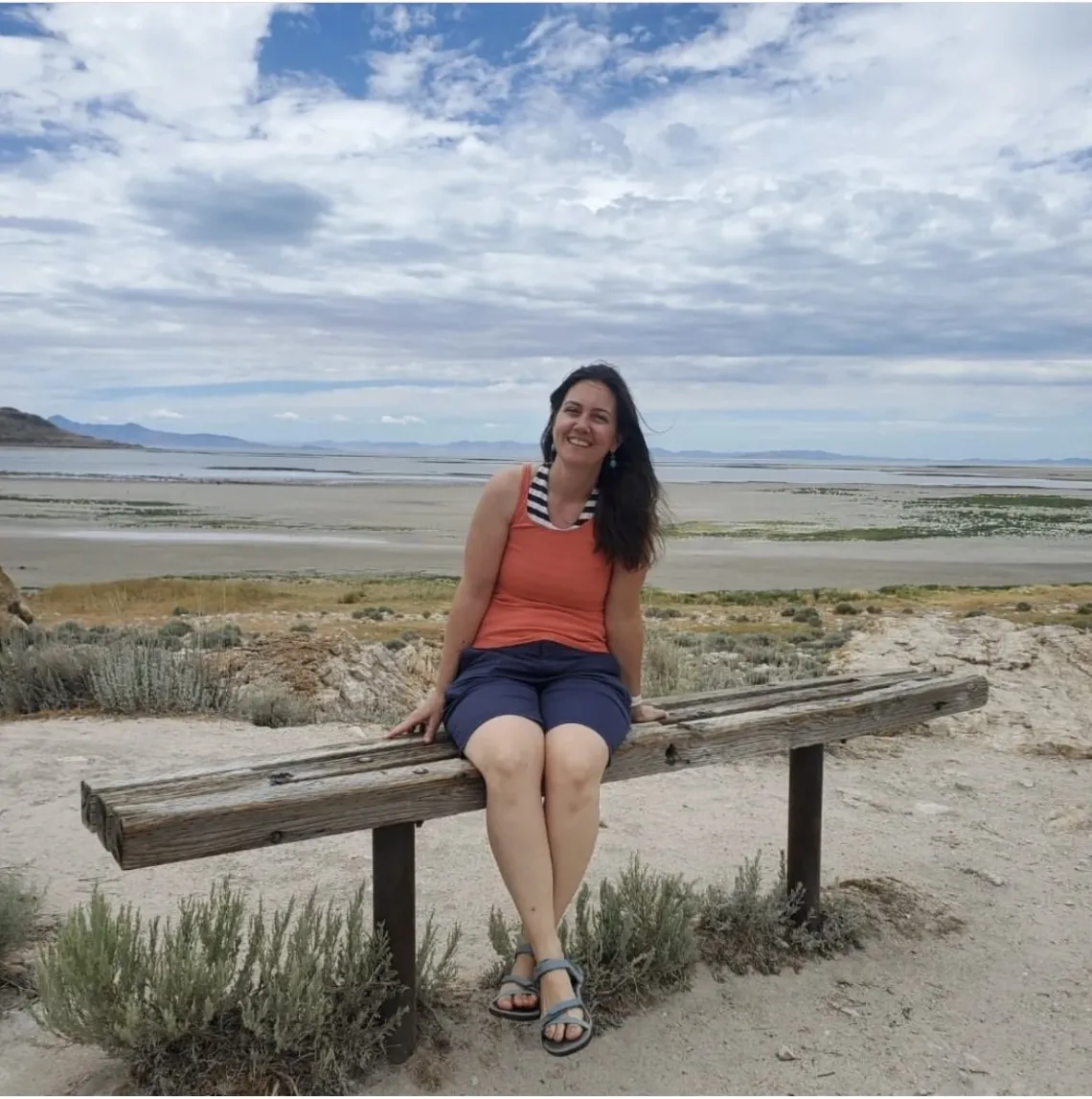 Nicole on a bench in front of sand and a body of water