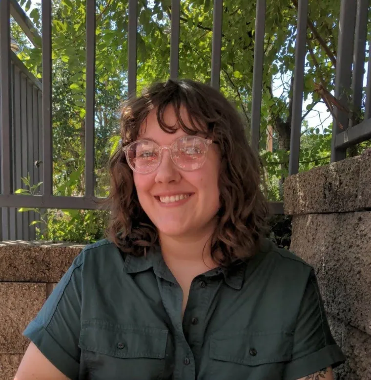 Erin in front of a brick wall, with foliage in the background