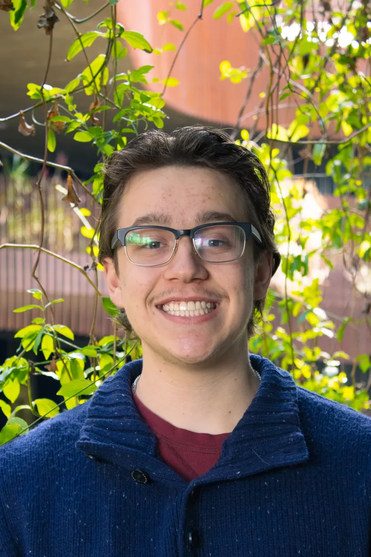 Allen in front of foliage, wearing a blue sweater and glasses