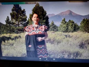 Ann Marie Chischilly giving a talk with trees and foliage behind her.